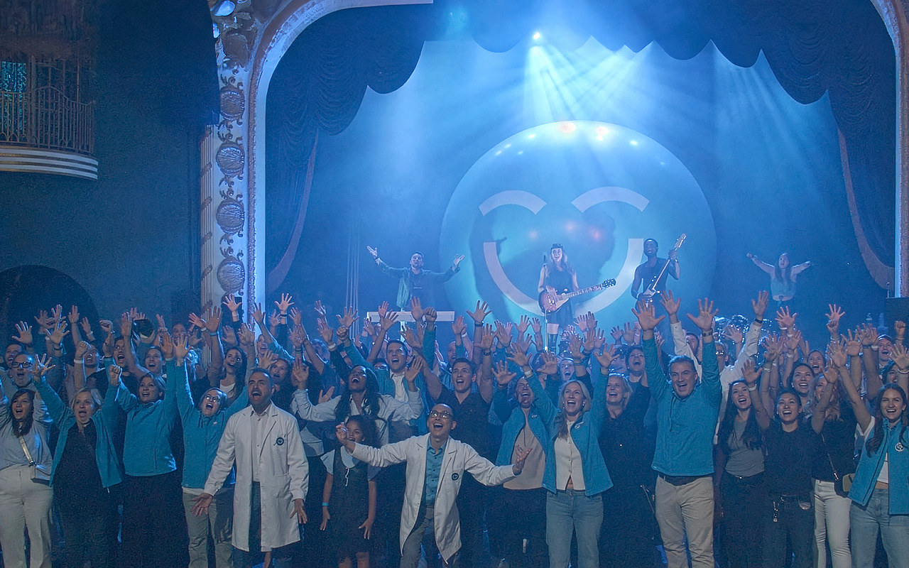 A lively crowd joyfully celebrates the launch of the "Smiles Across Canada" campaign, raising their hands in excitement. In the background, a performer plays guitar on stage, accompanied by colorful lighting and a large 123Dentist Smiley adding a playful touch to the atmosphere.