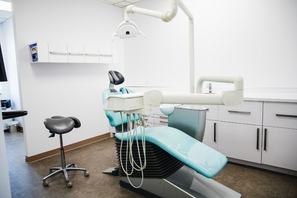 A modern dental office featuring a comfortable dental chair, a stool for the dentist, and bright, clean walls. The workspace is organized, emphasizing a hygienic environment. A friendly blue smiley face, known as the 123Dentist Smiley, adds a cheerful touch to the scene.