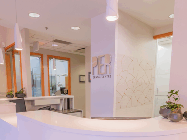 A modern dental office reception area featuring a sleek, white front desk with a logo reading "PIER Dental Center." Natural light floods through large windows, and decorative plants add a touch of greenery to the welcoming atmosphere.
