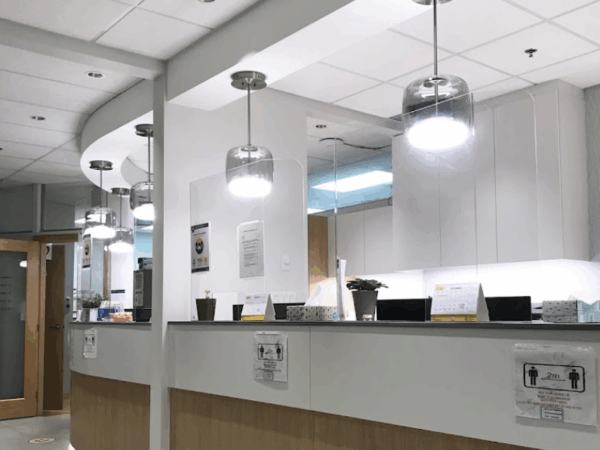 A modern reception area with a curved counter, illuminated by stylish pendant lights. The space features potted plants, informational signage, and a welcoming atmosphere typical of a healthcare facility.